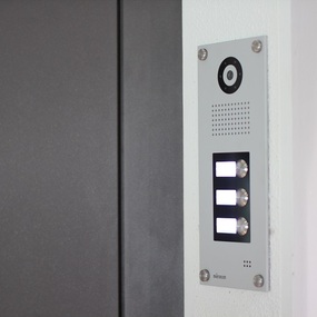 Moderne Gegensprechanlage mit Kamera und beleuchteten Klingeltasten an einer Haustür.