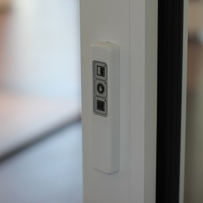 Bedienelement für elektrische Schiebetür an modernem, weißen Türrahmen im Innenraum.